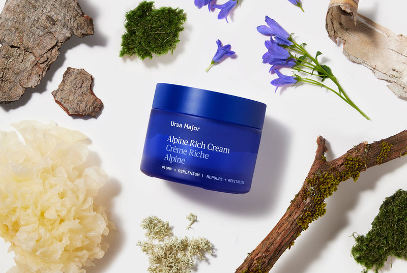 Blue jar of Alpine Rich Cream surrounded by natural elements on a white background