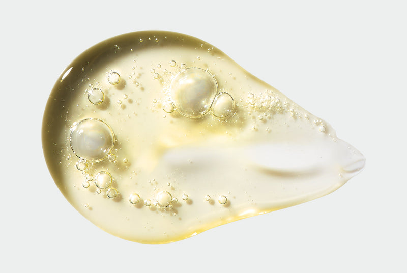 Close-up of a droplet of yellow Hand Wash with bubbles on a light gray background