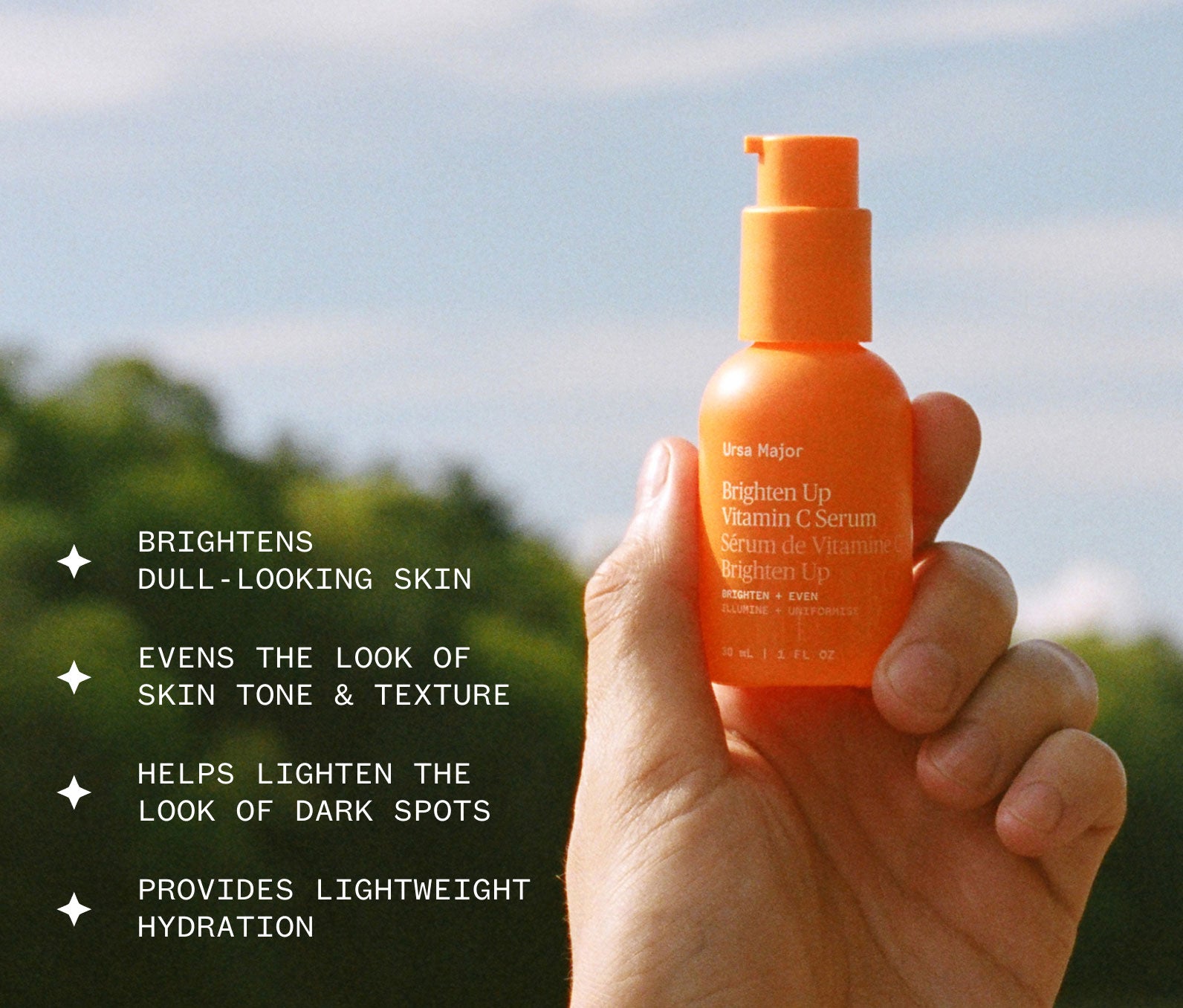 Orange Brighten Up Vitamin C Serum bottle held in a hand against a blurred natural background, with text about its benefits: Brightens dull-looking skin; Evens the look of sin tone and texture; Helps lighten the look of dark spots; Provides lightweight hydration