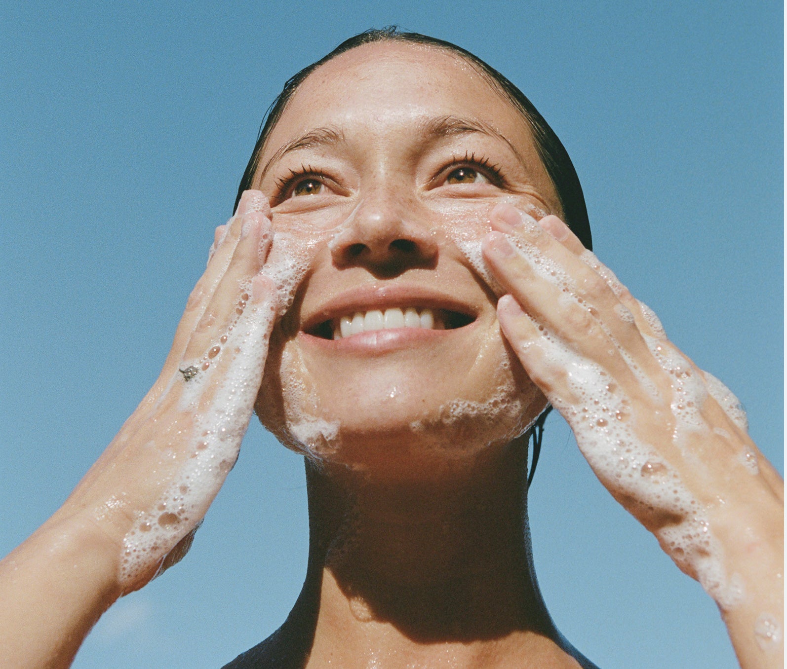 Smiling woman washing her face with a clear blue sky background