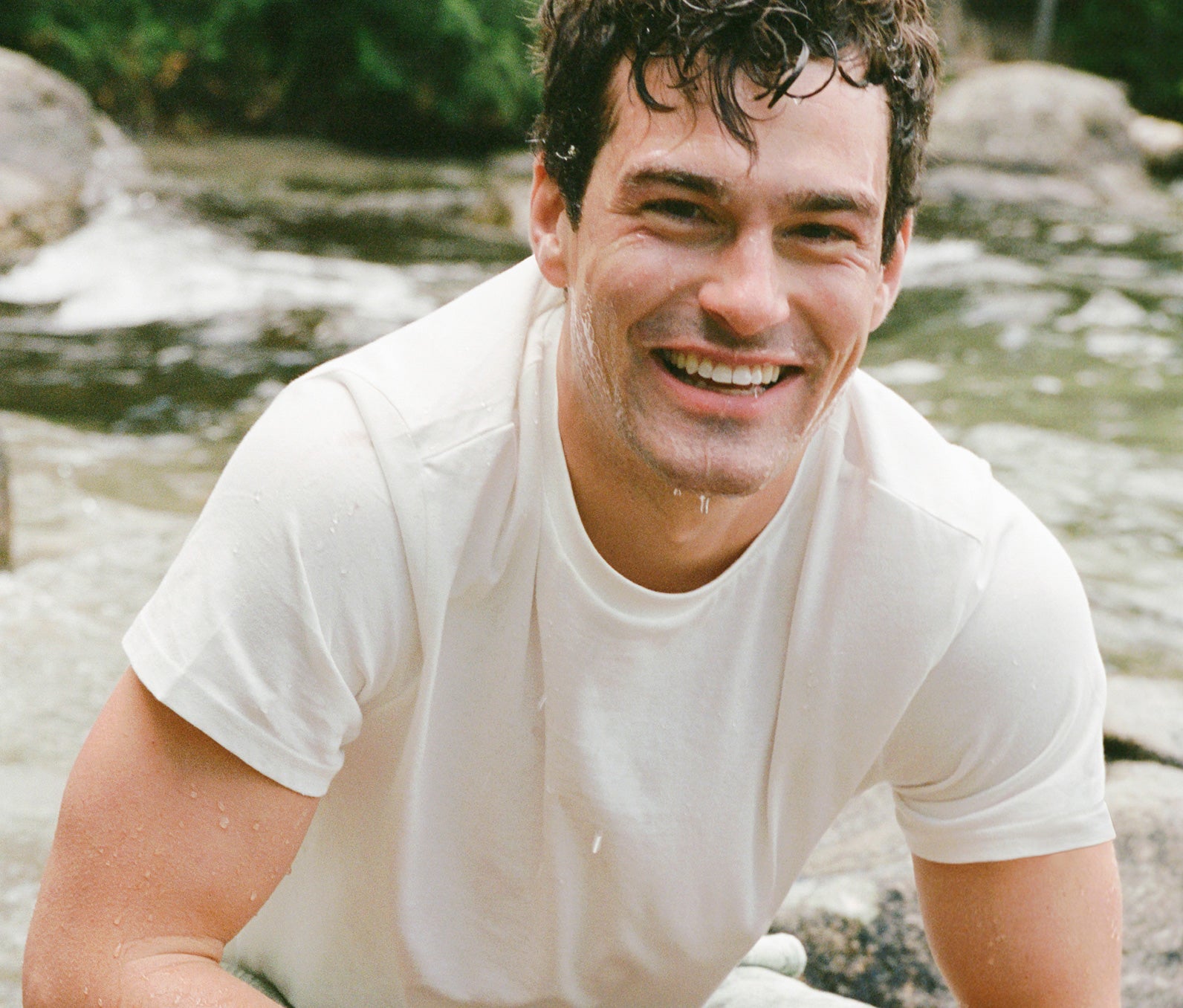 Man in a white t-shirt sitting by a stream with a natural background