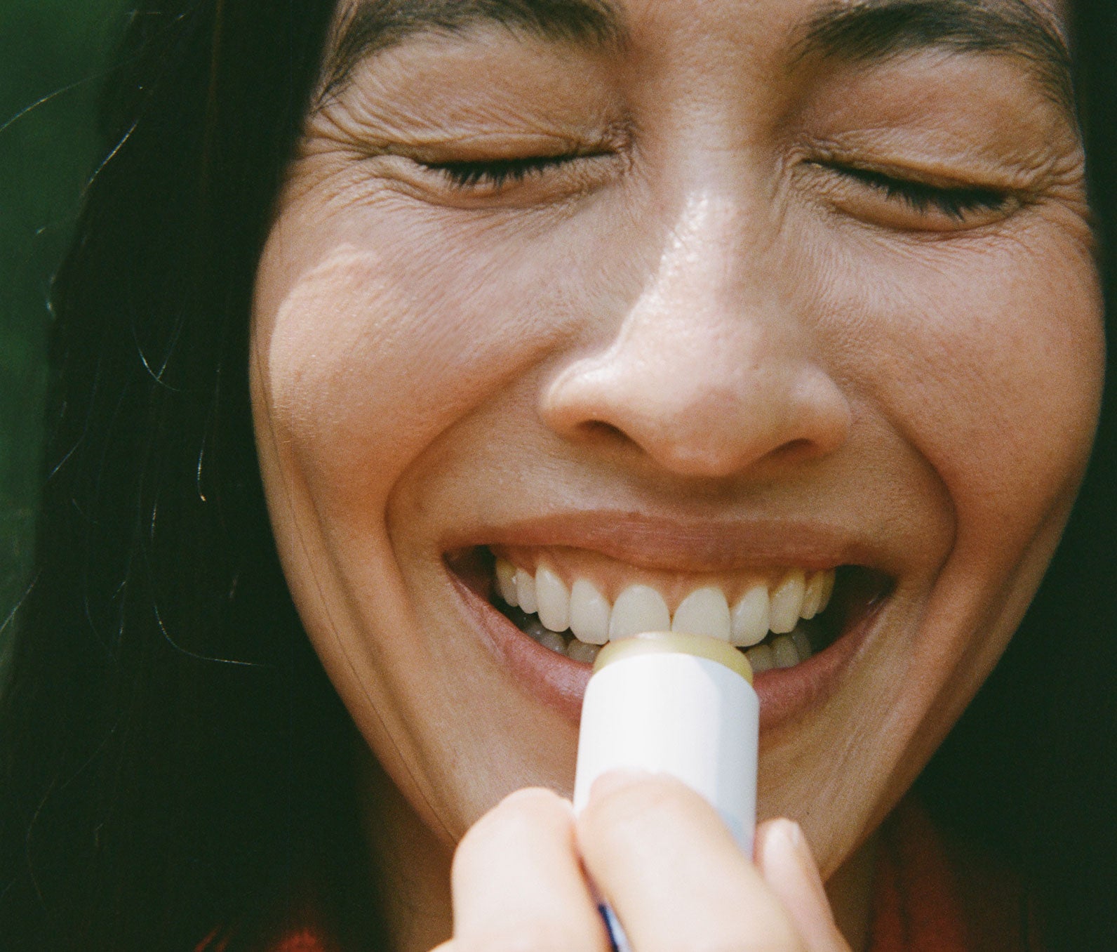 Close-up of a smiling woman applying Going Places Lip Balm with a blurred background