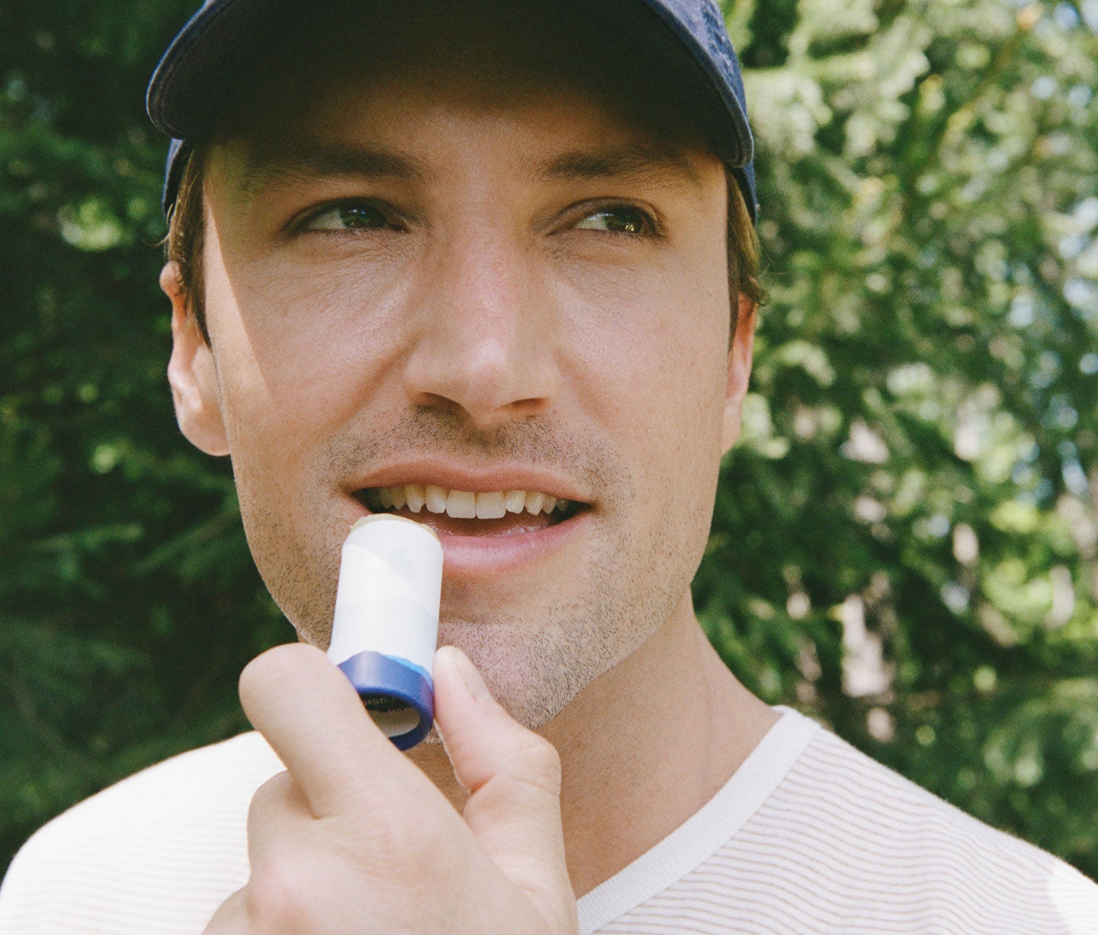 Man applying Going Places Lip Balm outdoors with greenery in the background