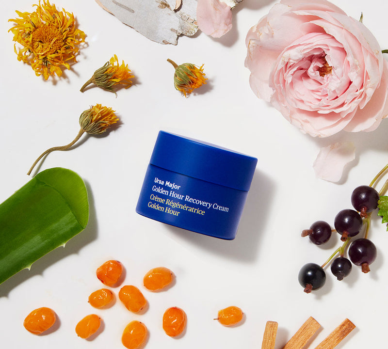 Small blue jar of cream surrounded by flowers and fruits on a white background