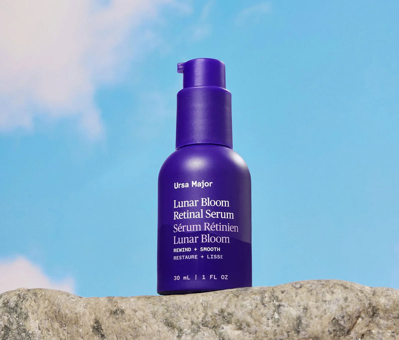 Purple bottle of Ursa Major Lunar Bloom Retinal Serum on a rock with a blue sky background