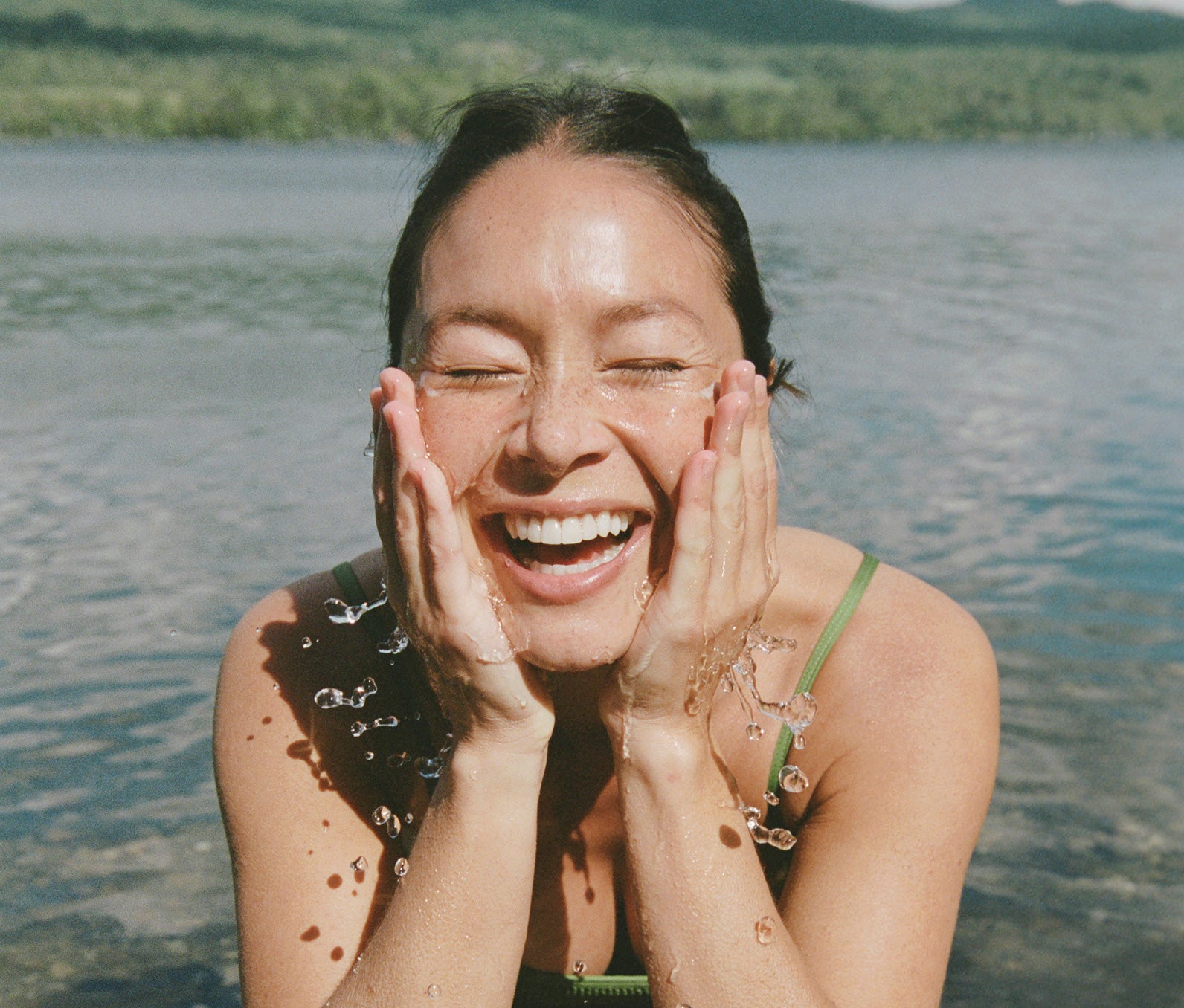 Woman washing her face and smiling in front of a lake