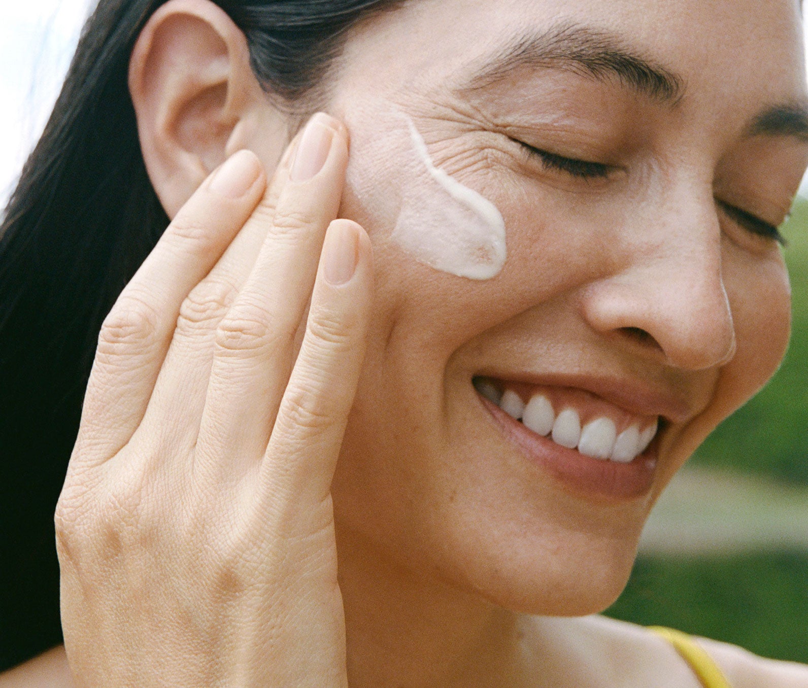 Smiling woman applying product to her face with a blurred natural background