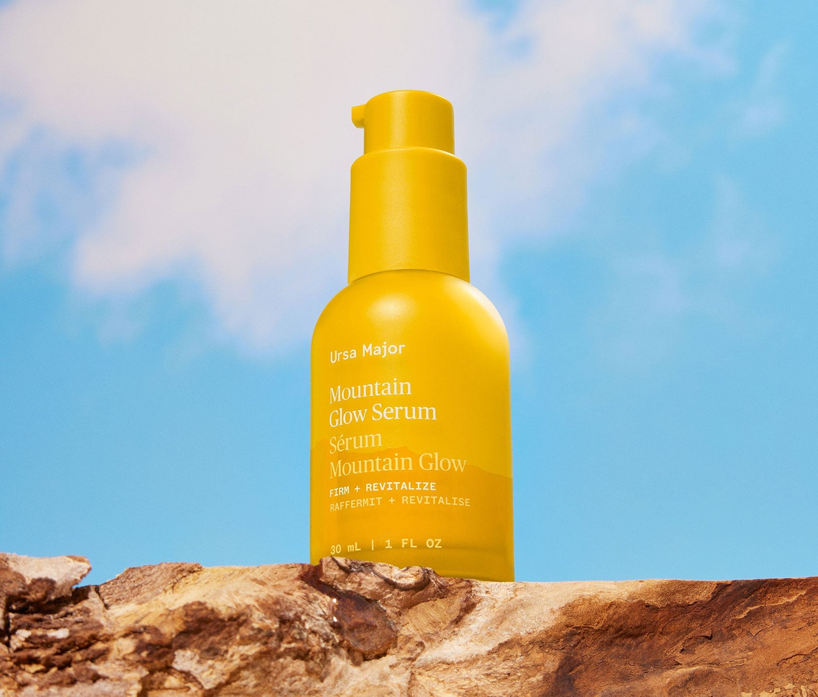 Yellow bottle of Ursa Major Mountain Glow Serum on a wooden beam with a blue sky background