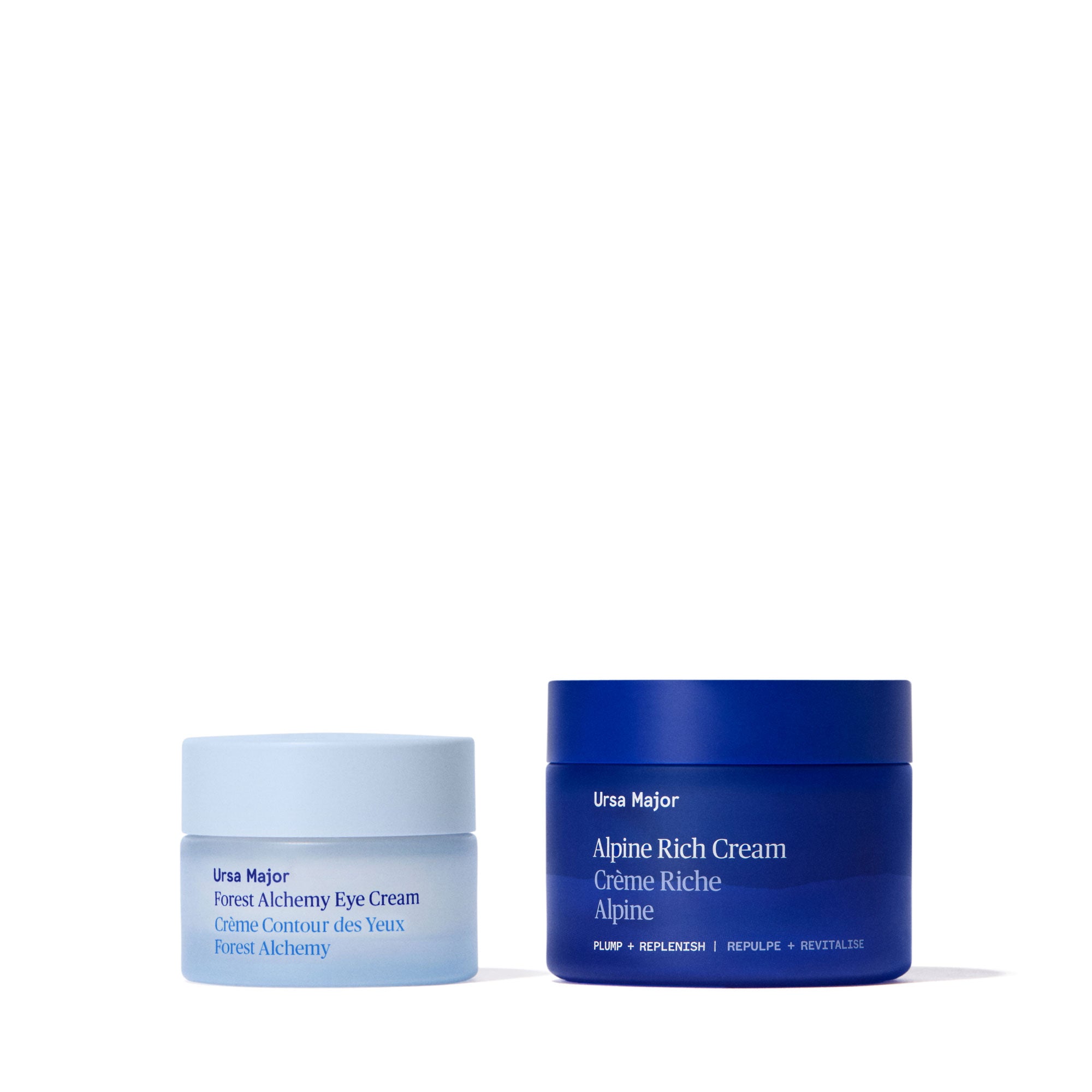 Smaller jar of light blue Ursa Major Forest Alchemy Eye Cream next to bigger, navy blue jars of Alpine Rich Cream on a white background