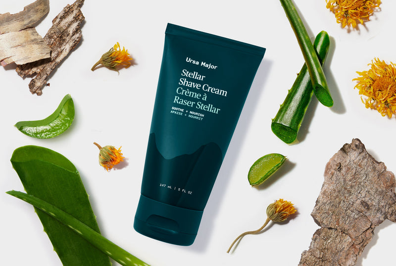 Green Ursa Major Stellar Shave Cream tube surrounded by natural elements on a white background