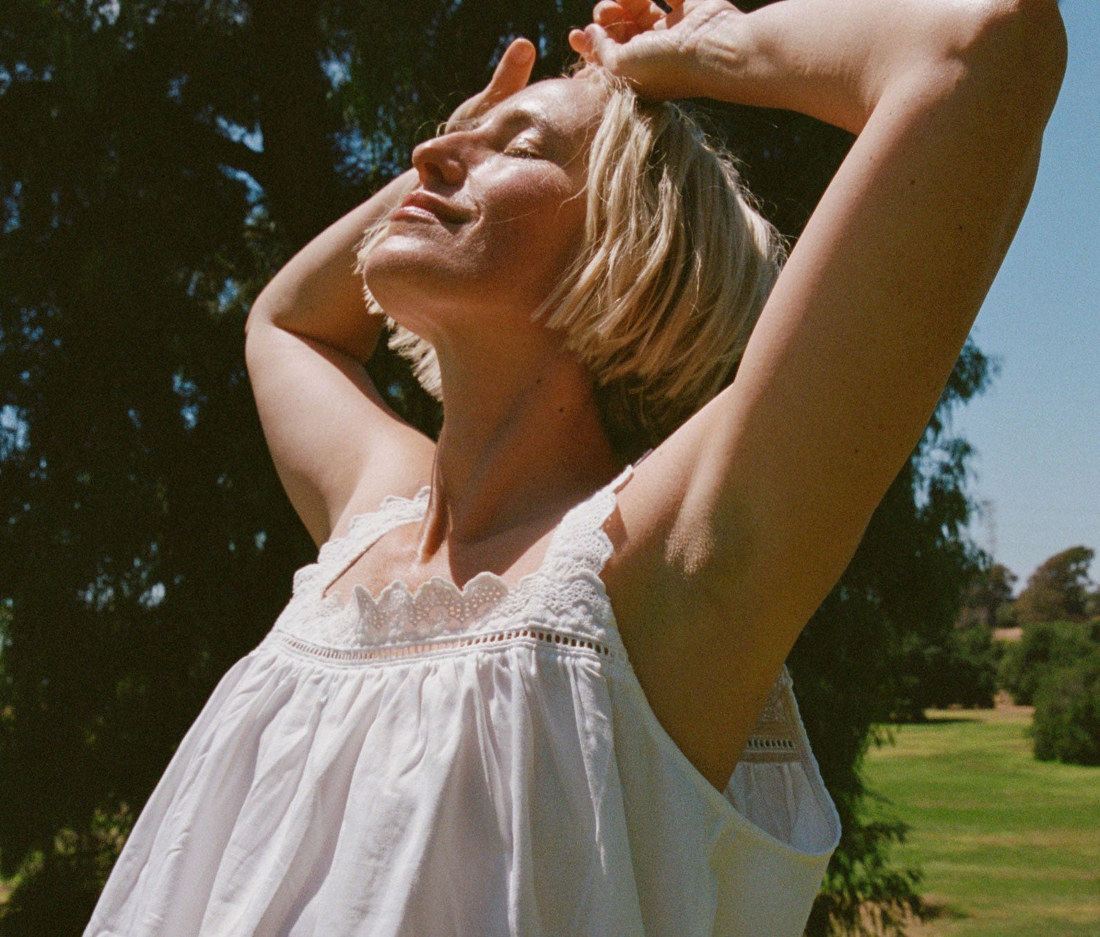 Woman in a white dress standing outdoors with trees and sky in the background.