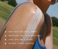 Person applying Golden Hour Body Serum to shoulder against a green outdoor background with text highlighting product benefits, including: Helps skin look firm and smooth; Revitalizes dull, lackluster skin; Even skin tone and texture; Delivers lasting hydration