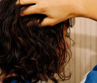 Close-up of a person with curly hair applying Golden our Dry Oil to their hair.