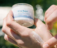 Person holding a jar of Ursa Major Alpine Rich Cream  and swiping some on their hand.