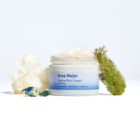 Open jar of Ursa Major Alpine Rich Cream on a white background with ingredients around it. 