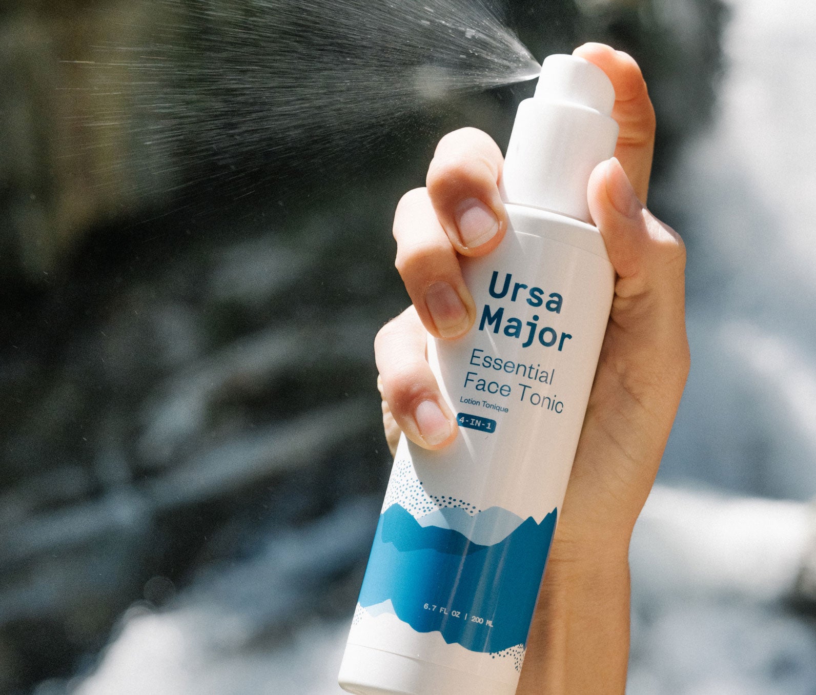 A woman's hand holding a spray bottle of Ursa Major Essential Face Tonic, a 4-in-1 tonic for face