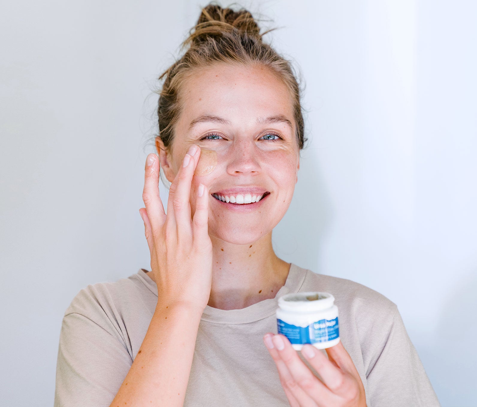 Woman smiling in front of a white wall swiping on Bright & Easy 3-Minute Flash Mask.