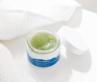 Open jar of Bright & Easy 3-Minute Flash Mask on a white table with a white towel.  Inside the jar is the mask that's a pale-green color.