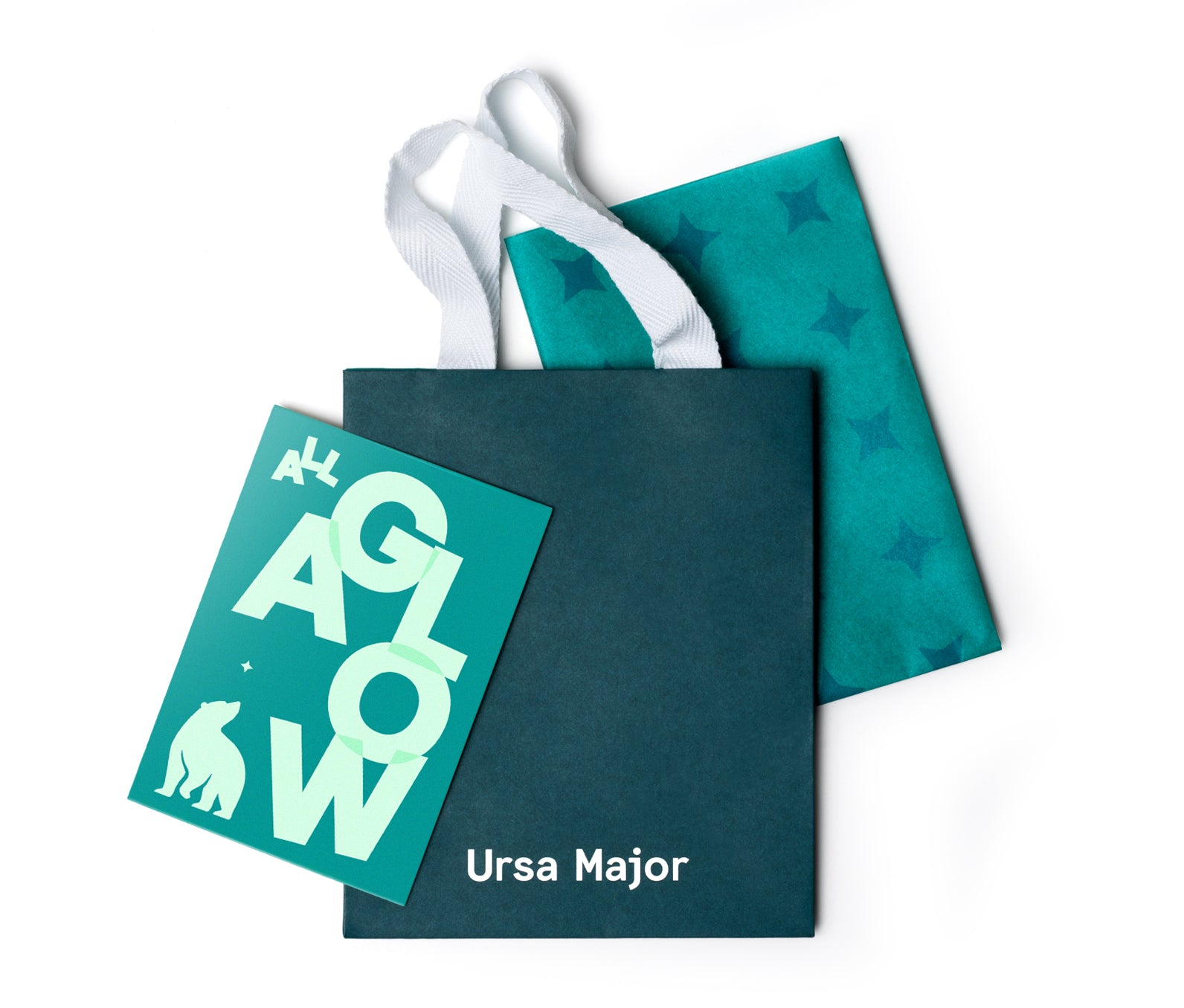 Teal gift bag with 'Ursa Major' on it with a 'All a Glow' card and teal tissue paper on a white background.