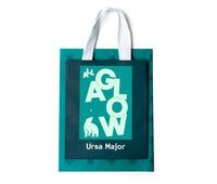 Teal gift bag with 'Ursa Major' on it with a 'All a Glow' card and teal tissue paper on a white background.