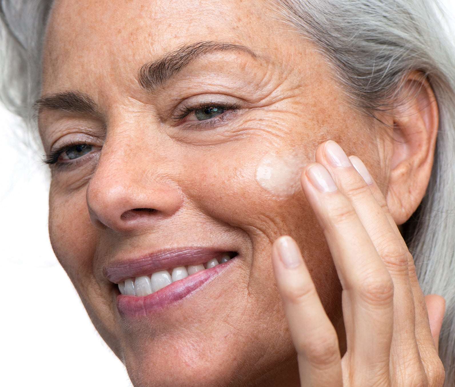 Elderly woman applying a drop of vitamin C serum to her cheek, highlighting its brightening effect on her radiant skin.
