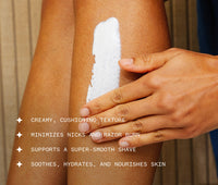 Hand applying Ursa Major Stellar Shave Cream to their leg.  Text on image reads that the product has a creamy, cushioning texture, minimizes nicks and razon burn, supports a supersmooth shave, soothes, hydrates, and nourishes skin.