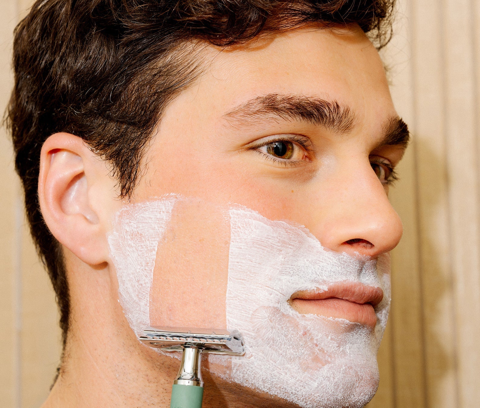 Man shaving his face with a razor and Ursa Major Stellar Shave Cream.