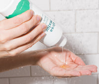 Hands pouring a bottle of Ursa Major Citrus Riot Body Wash into their hands in a shower.