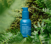 Jar of Ursa Major Forest Water Hyaluronic Serum outside in a green forest.