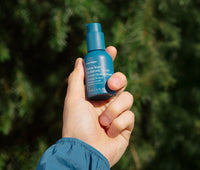 Hand holding a jar of Forest Water Hyaluronic Serum outside with sun shining on it.