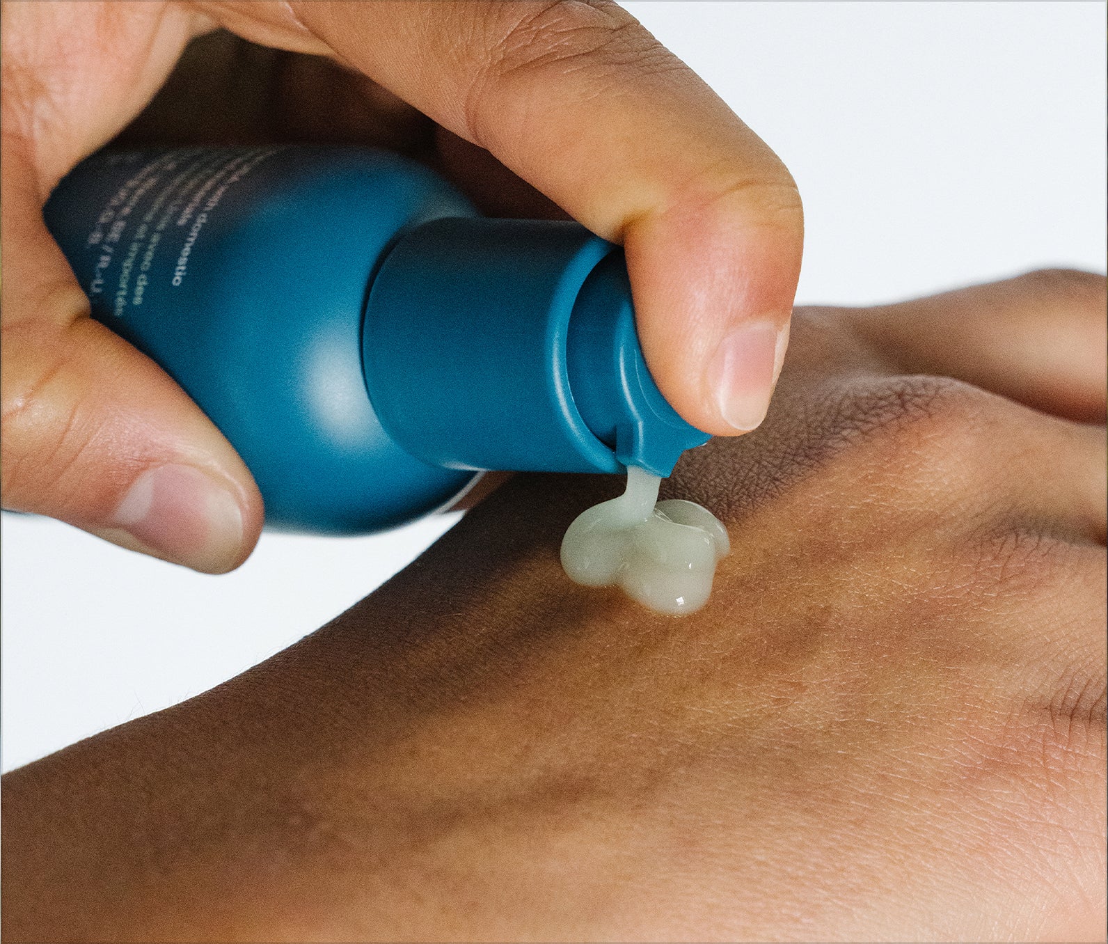 Hands pumping Ursa Major Forest Water Hyaluronic Serum onto the back of their hand. Serum is a light-green color.