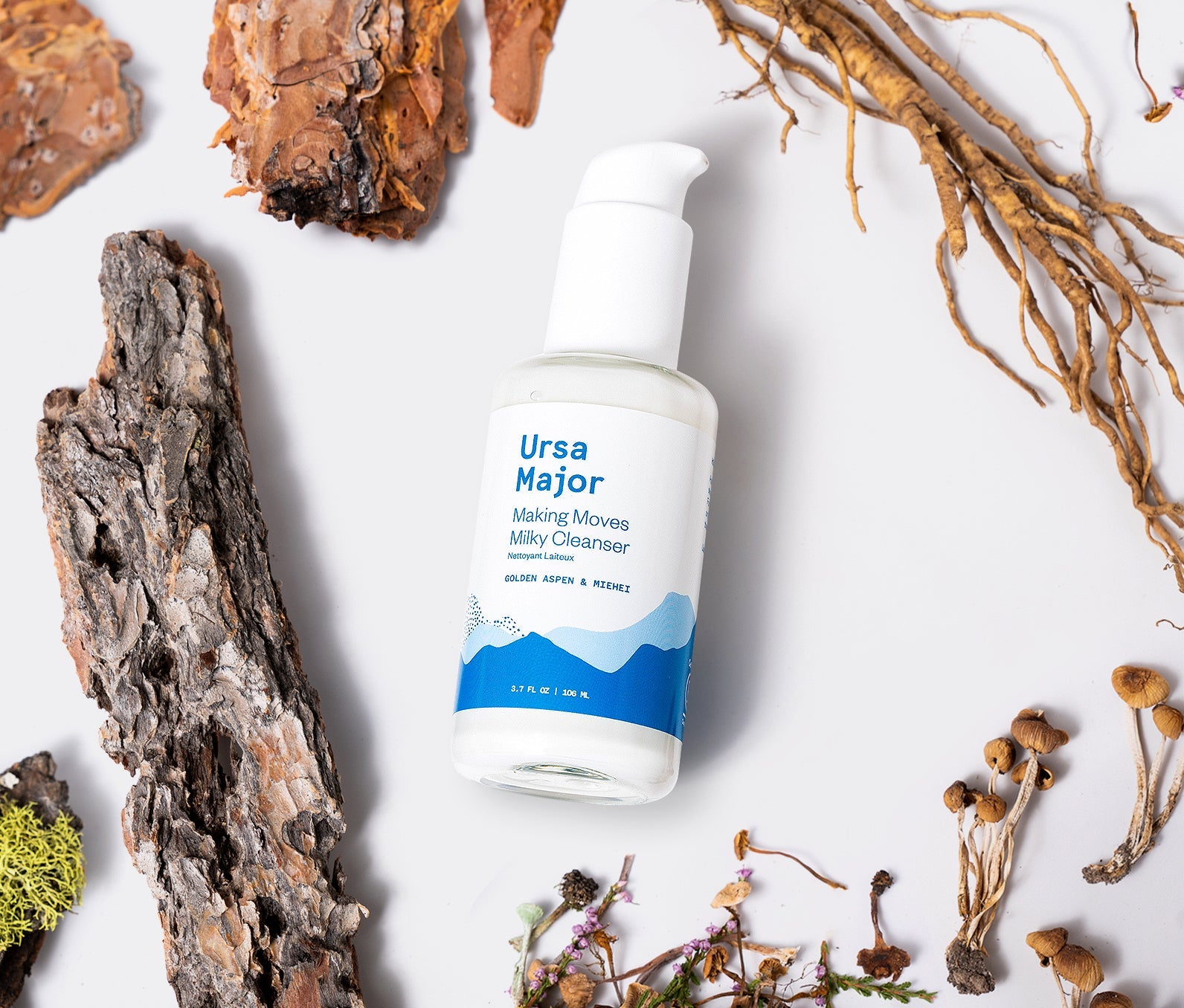Bottle of Ursa Major Making Moves Milky Cleanser on a white background surrounded by some of the product's natural ingredients.