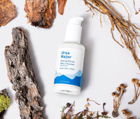 Bottle of Ursa Major Making Moves Milky Cleanser on a white background surrounded by some of the product's natural ingredients.
