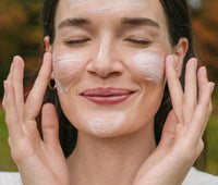 Smiling woman applying creamy mask to her face with a blurred natural background