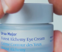 Video of person opening up jar of Ursa Major Forest Alchemy Eye Cream, picking up a dab of rich, beige cream with their finger, then gently smoothing onto skin 