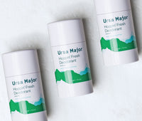Aerial shot of three tubes of Ursa Major Hoppin' Fresh Deodorant on a white textured background.