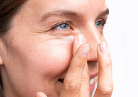 Close-up of a woman putting Ursa Major Forest Alchemy Eye Cream under her eyes with her finger.