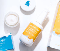 Mountain Glow Golden Serum and an open jar of Forest Alchemy Eye Cream on a white backroom counter.
